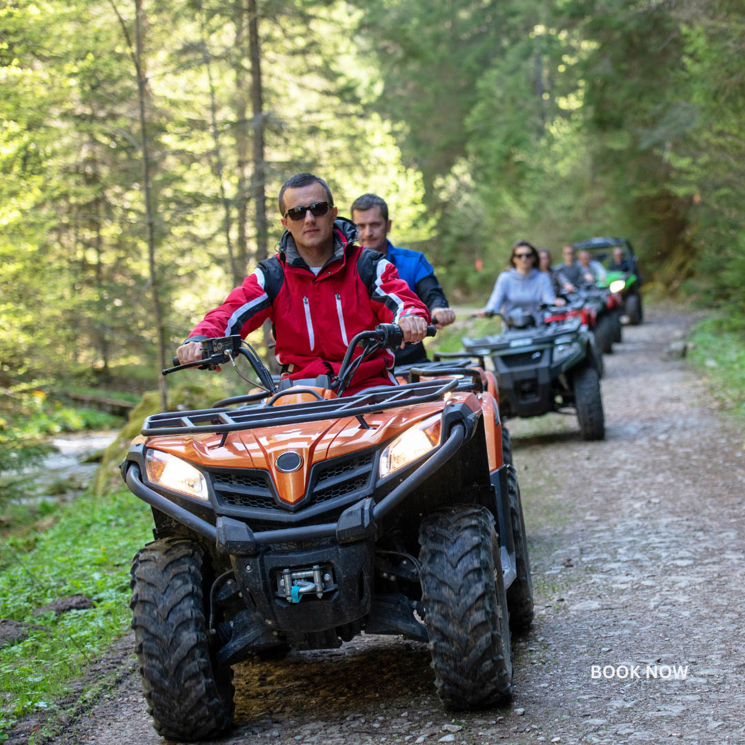 A group rides ATVs on a forest trail, led by a person in a red jacket - https://jmsullivaninsurance.com/